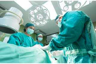 Three surgeons wearing green surgical gowns working on a patient in an operating theatre