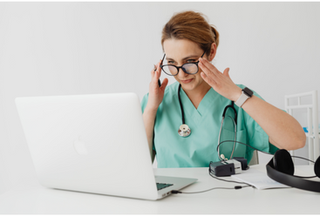 Healthcare professional in green scrubs looking at a laptop screen