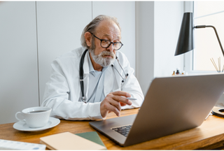 Doctor wearing a white coat and stethoscope around their neck looking at a laptop screen