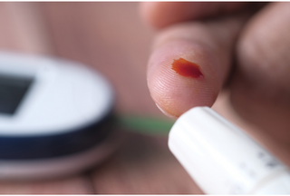 A close up of a finger with a drop of blood after a pin-prick test
