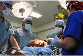 Four surgeons wearing surgical gowns working on a patient in an operating theatre
