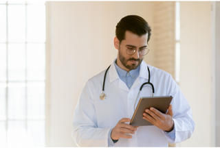 Doctor wearing a white coat and stethoscope looking at a tablet device